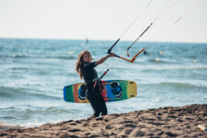 Woman holding kiteboard and going into the water to kitesurf on a beautiful beach.