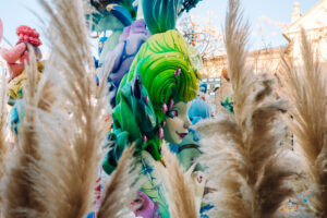 A vibrant ninot figure stands in Valencia, surrounded by ornamental plants, showcasing intricate details and vivid colors during the famous Fallas festival.